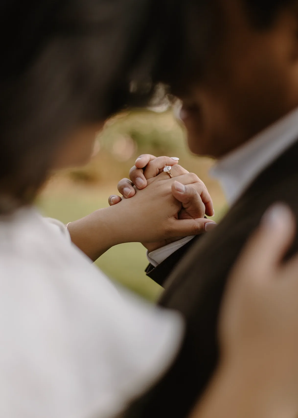 Their clasped hands and ring framed by the blurred couple