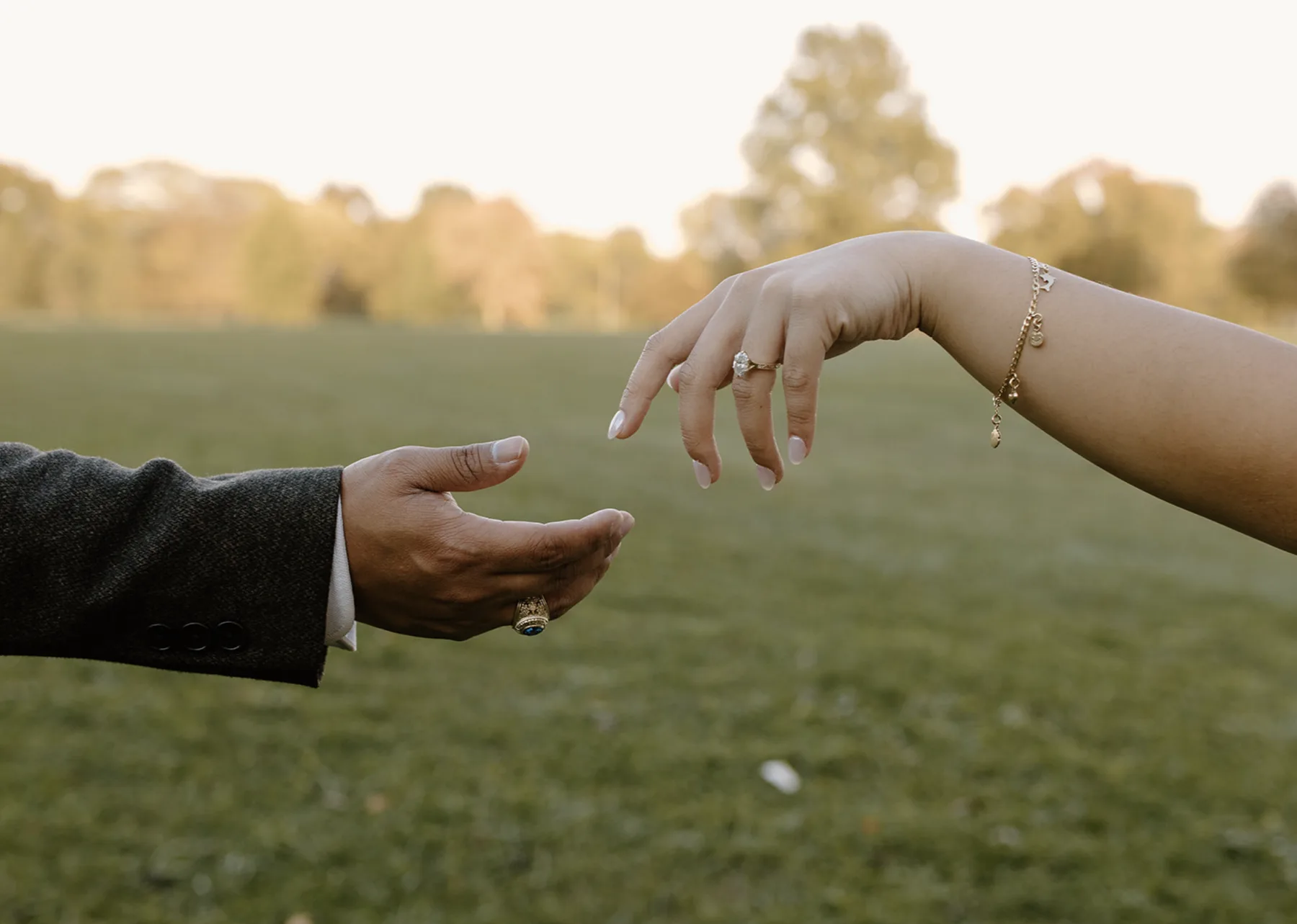Their hands reaching for each other over a field, her ring catching the light