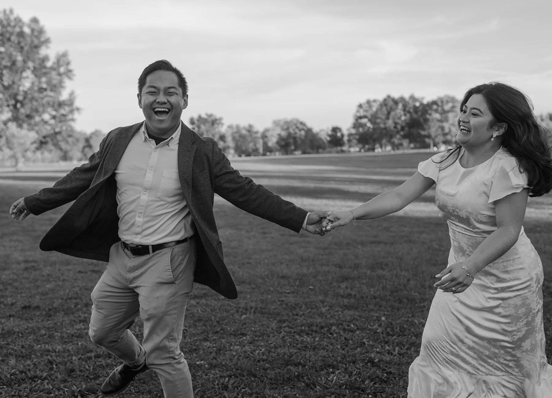 Black-and-white of the couple running hand in hand across a field, laughing