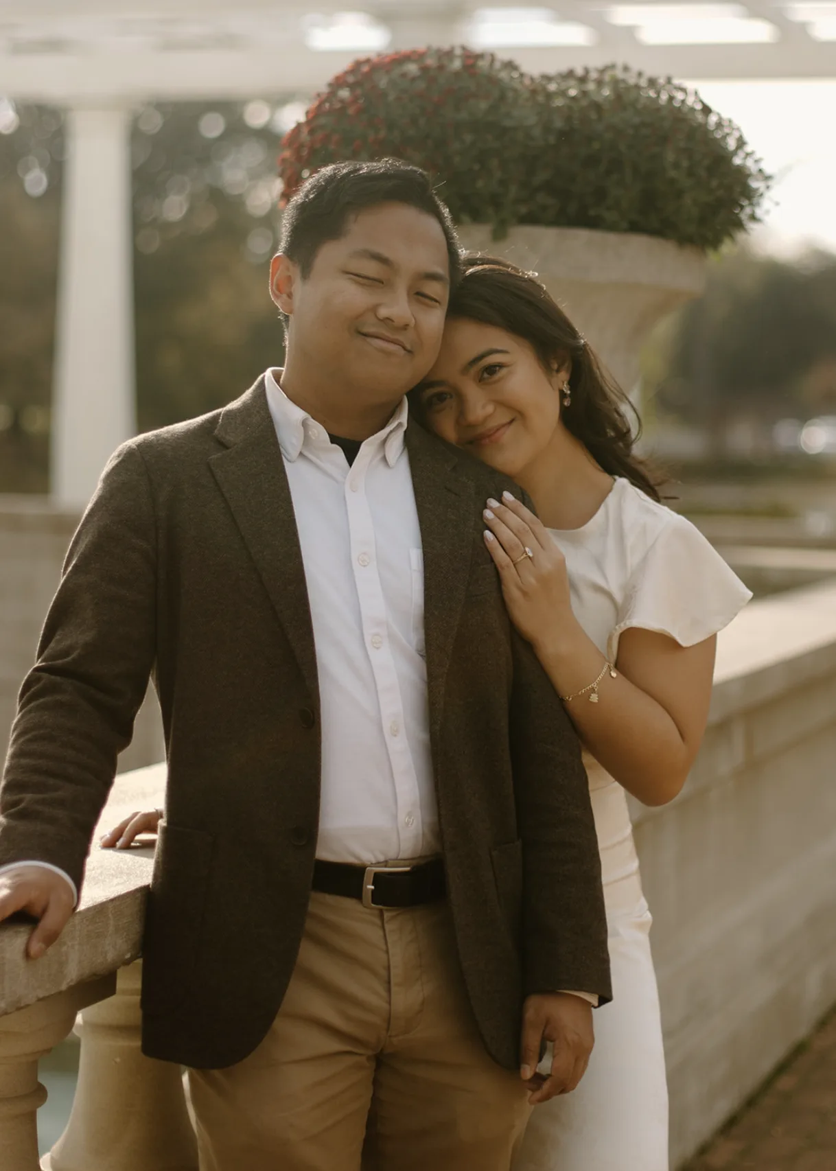 Carmela resting on CQ's shoulder at a garden balustrade in golden light
