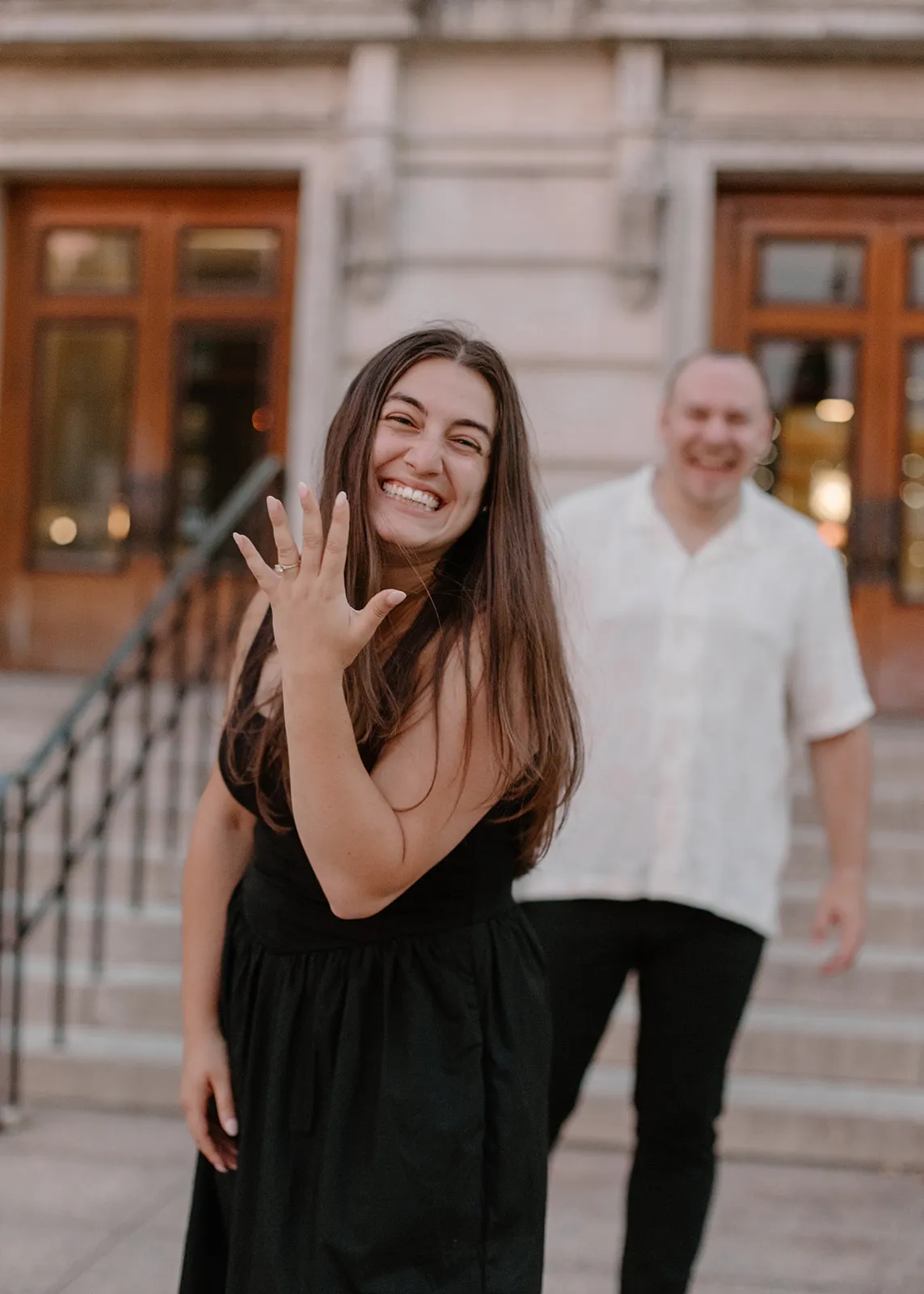 Gina laughing and showing her ring as Jacob walks up behind her
