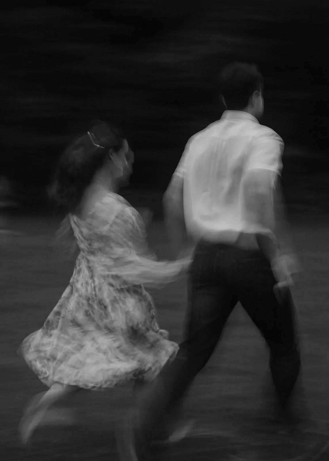 Black-and-white motion blur of a couple running hand in hand, her floral dress swirling